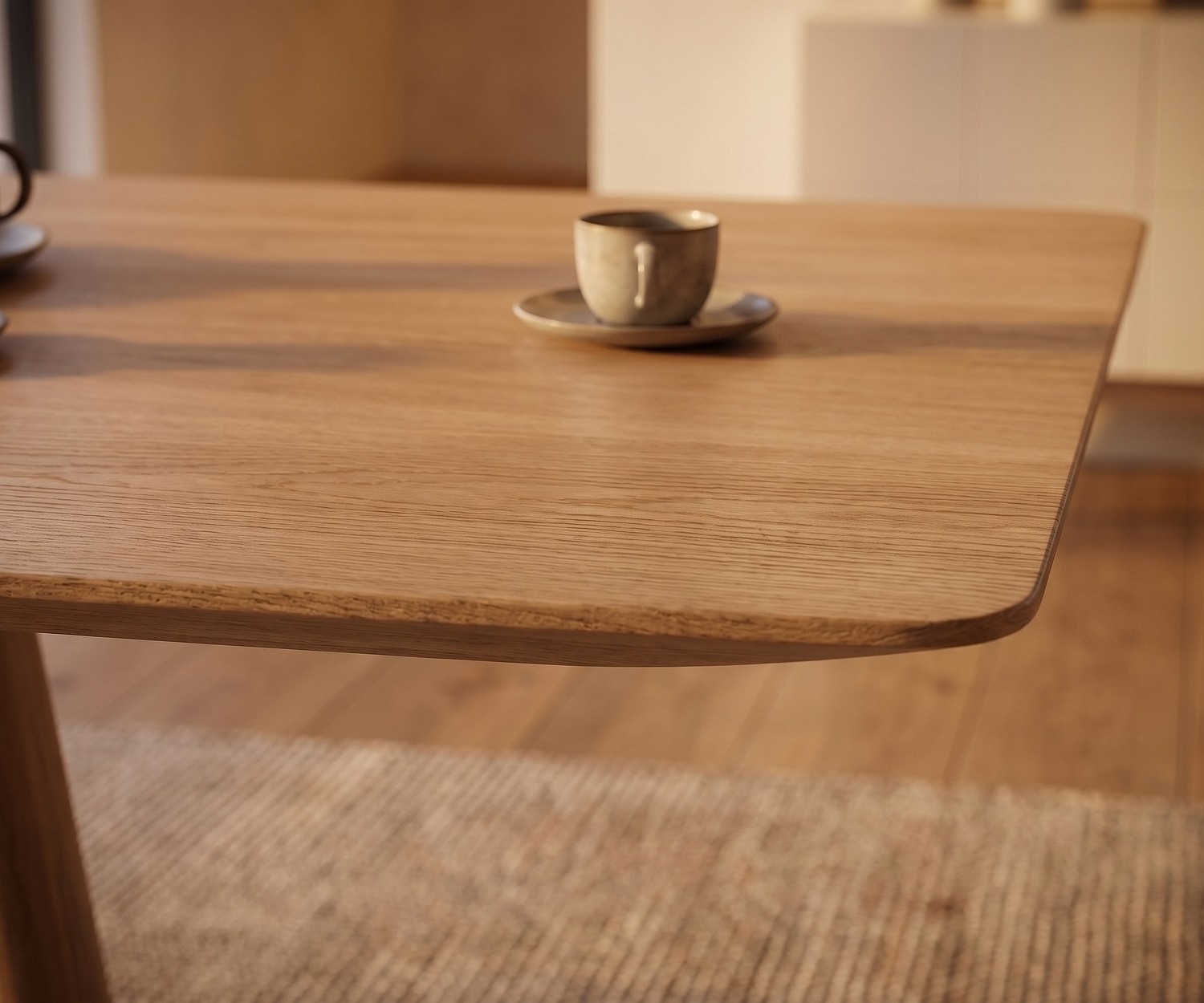 Table de repas en chêne al2 mos-i-ko aux angles arrondis Table de repas mos-i-ko 001 a en chêne clair, zoom sur le coin arrondi du plateau en bois dans une salle à manger moderne.