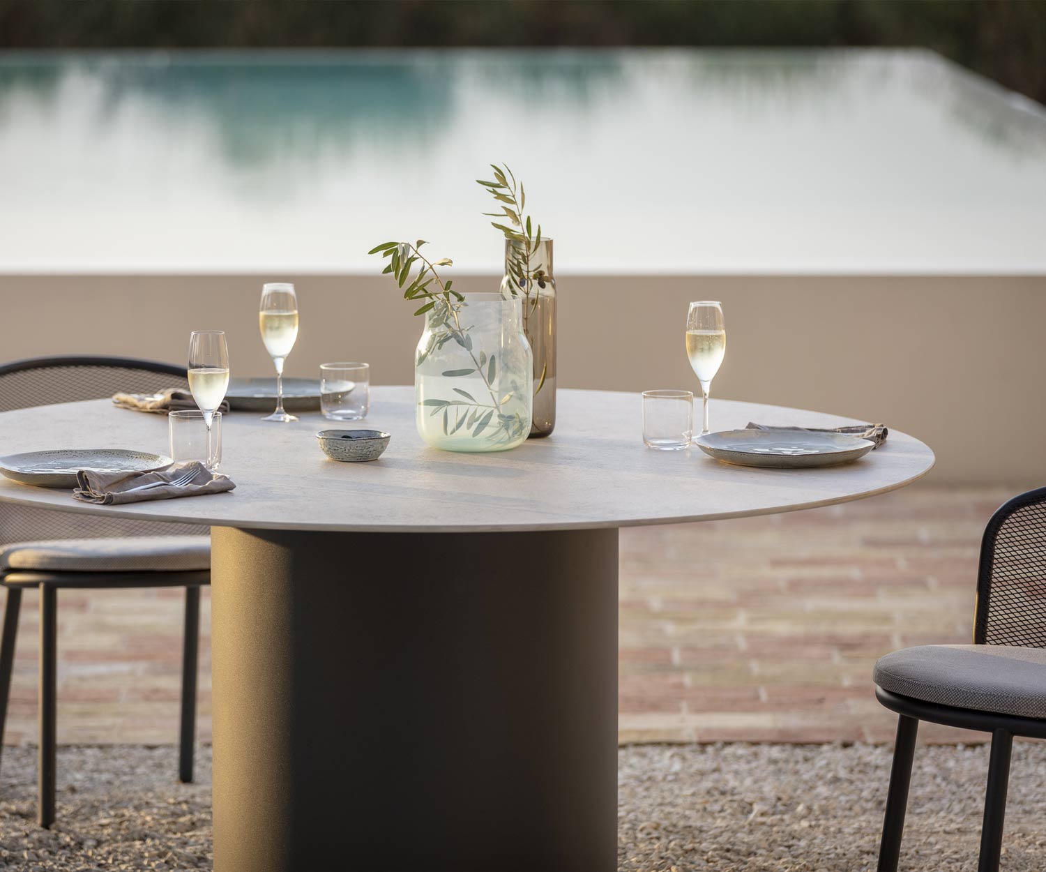 Table de salle à manger couverte de Todus avec plateau de table en céramique grise au bord de la piscine sur une terrasse de gravier Table de salle à manger couverte de Todus avec plateau de table en céramique grise au bord de la piscine sur une terrasse de gravier